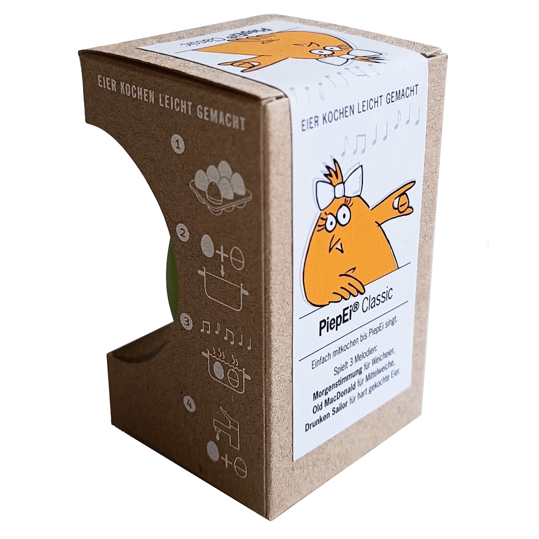 Braune PiepEi®-Classic-Kartonverpackung, schräg von vorn. Vorderseite: Cartoon-Huhn mit Schleife, 3 Melodien für weich/mittel/hart. Seitenwand mit Kochschritten; grüner Inhalt sichtbar.