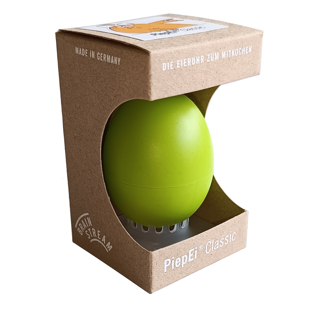 Helles, grünes Piep-Ei Classic in brauner, oben offener Kartonverpackung. Sichtbar: „MADE IN GERMANY“, „DIE EIERUHR ZUM MITKOCHEN“, „Brain Stream“ und „PiepEi Classic“. Spielt Melodien für weiche, mittlere oder harte Eier.